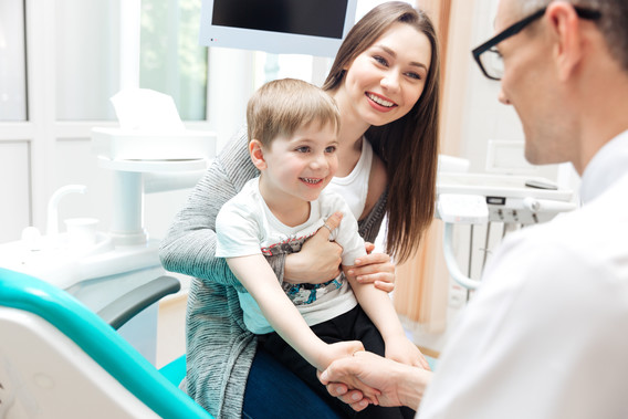 Happy mother and little boy talking to dentist in dental clinic