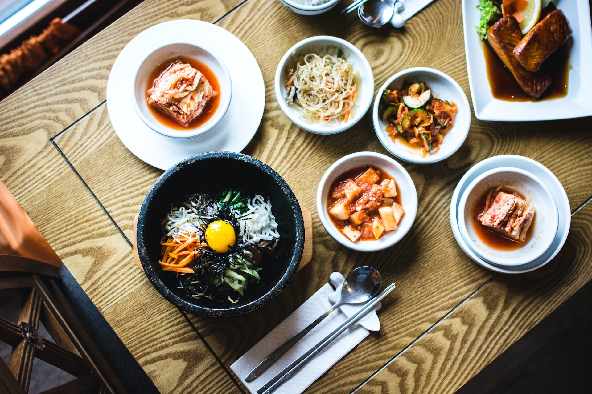 Korean specialties like kimchi and bibimbap arranged on a wooden table.