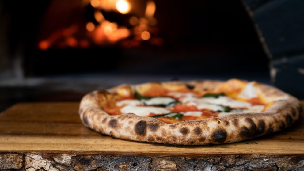 Pizza on a board, charcoal oven in the background.