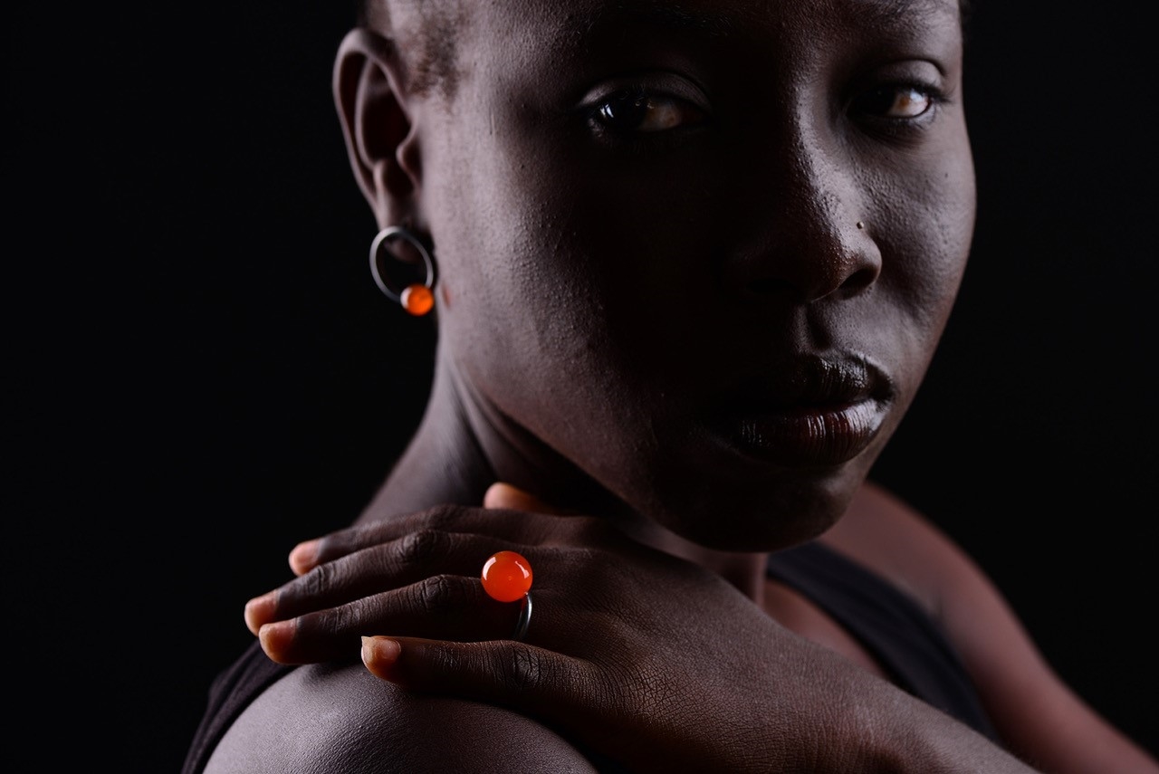 Weibliche Person of Colour trägt knallrote Ohrringe und Ring von Sofia Beilherz