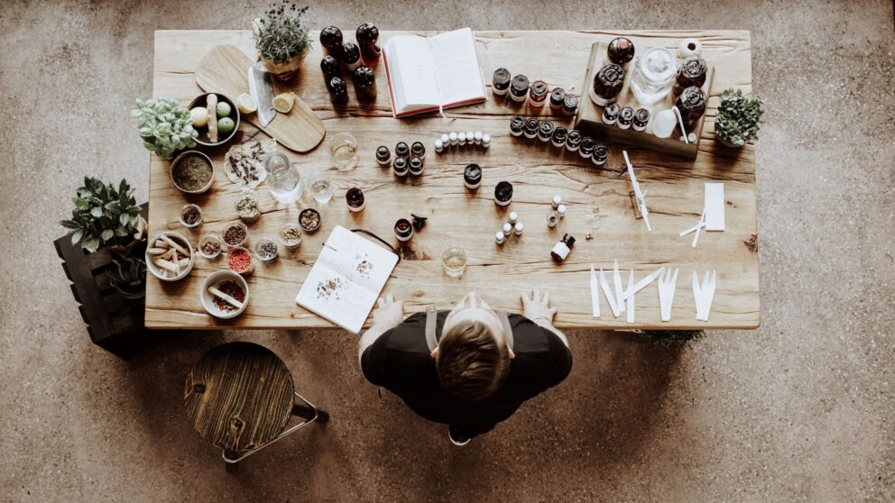 Wooden table photographed from above, with dried plants, jars, small bottles and a man standing at the table.