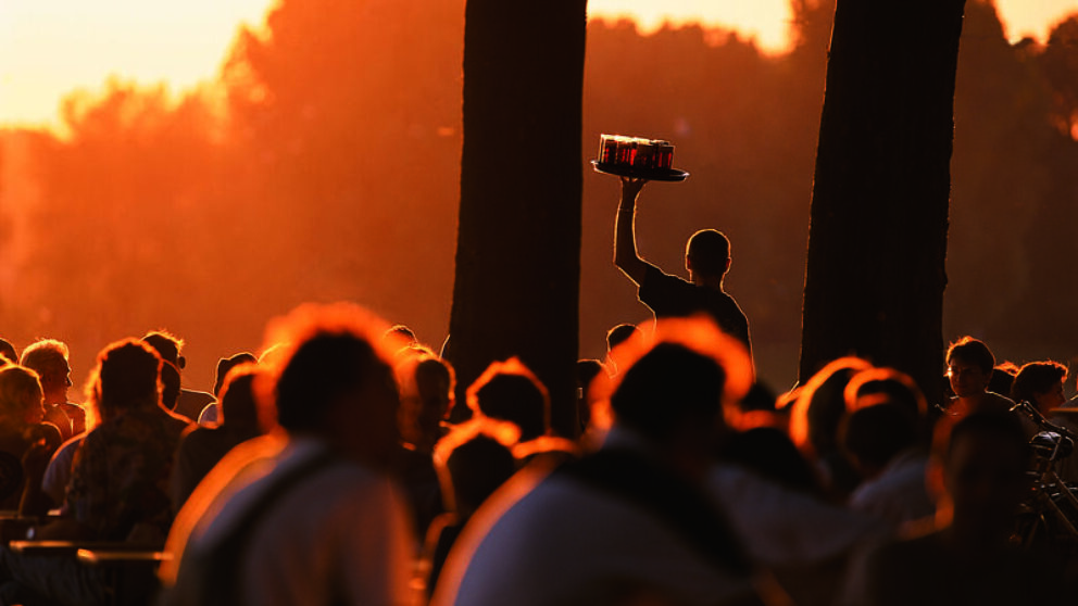 You can see a crowd of people silhouetted in the sunset, an arm with a tray of Altbier stands out.