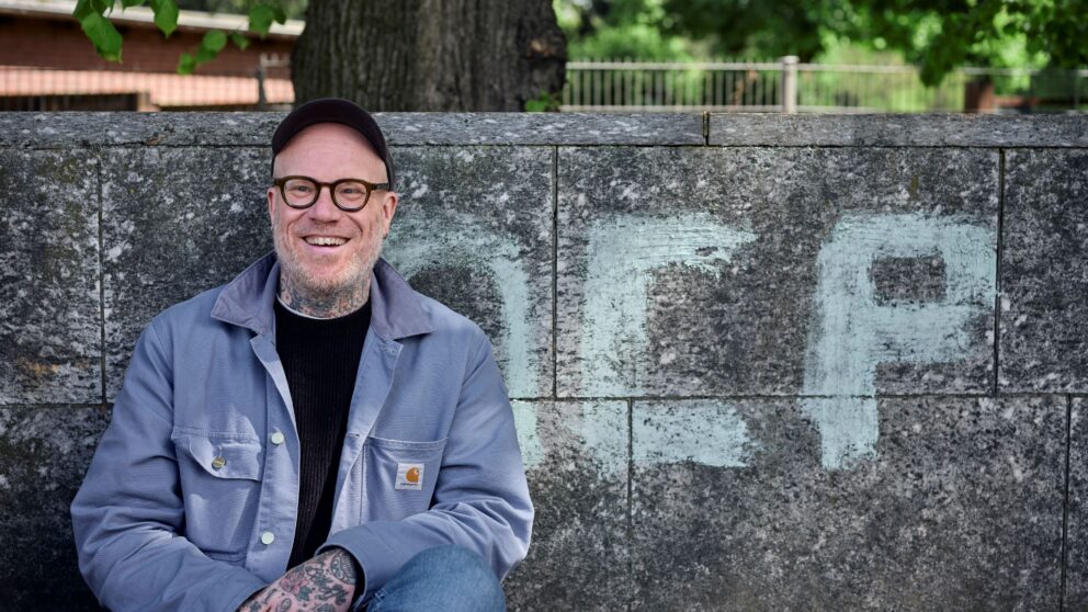 Artist Tim Berresheim sits on a stone bench with a wall in the background.