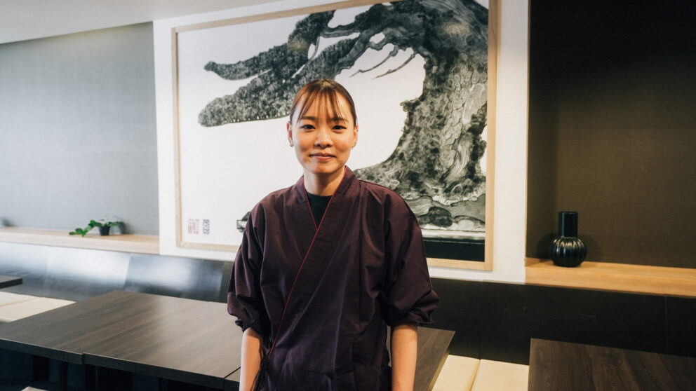 Soba master Tamaki Hamano in the Soba-An restaurant in front of a picture on the wall.