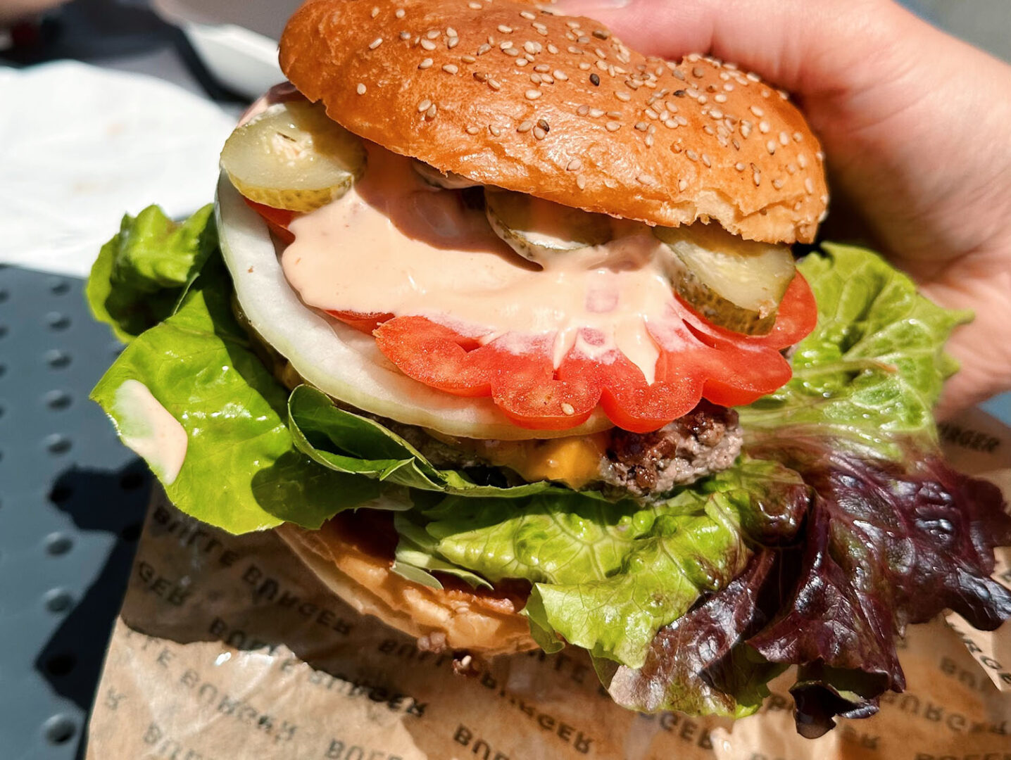 Burger, die obere Hälfte des Burgers ist so verschoben, dass man Dressing, tomate, Fleischpatty und Salatblatt sieht.