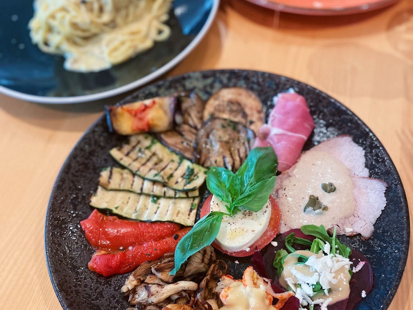 Man sieht einen Teller Antipasti auf einem Holztisch.