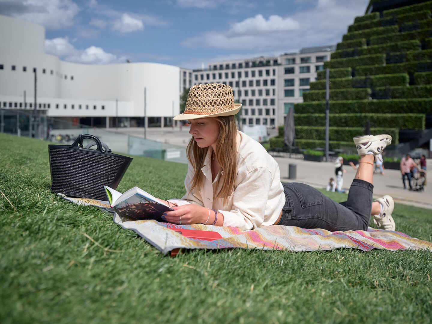A woman in a hat is lying on her stomach on a blanket on the sloping lawn at Gustaf-Gründgens-Platz.