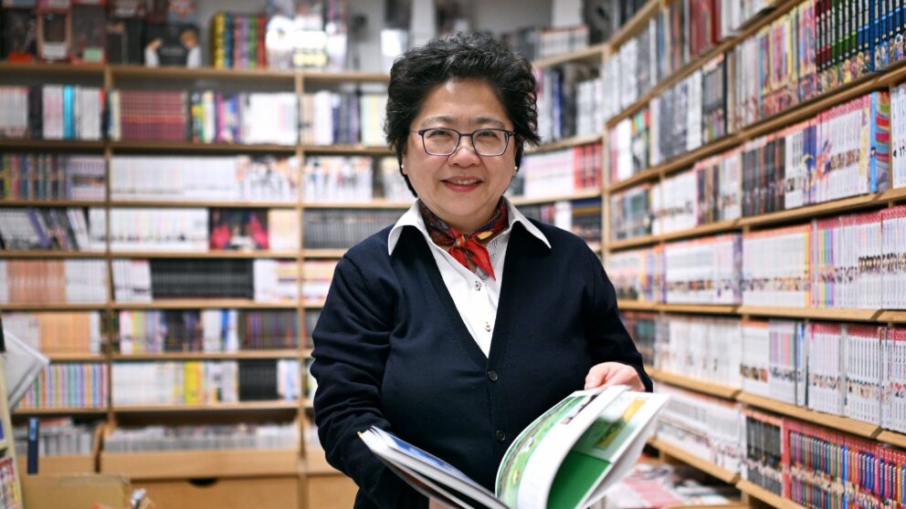 Yurie, owner of the Japanese bookshop Takagi Düsseldorf, is standing in the store holding an open book in her hands.