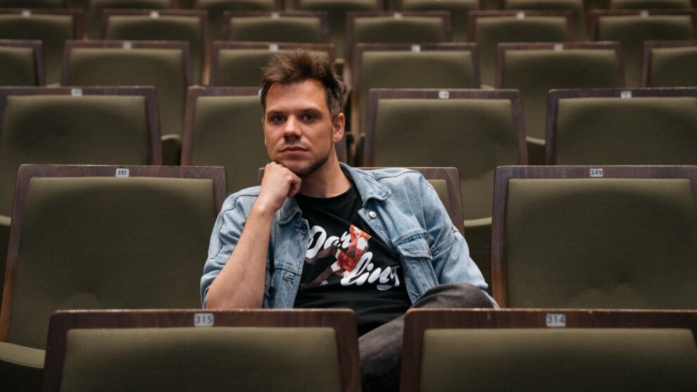 Alle Rhein mit Lasse Scheiba. Er sitzt auf dunkelgrünen Sitzen im Zuschauerraum im Düsseldorfer Schauspielhaus.