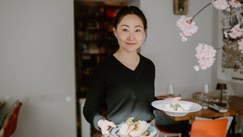 Dim Sum Restaurant Hashi. Man sieht die Inhaberin mit zwei Tellern, auf denen Dim Sums angerichtet sind.