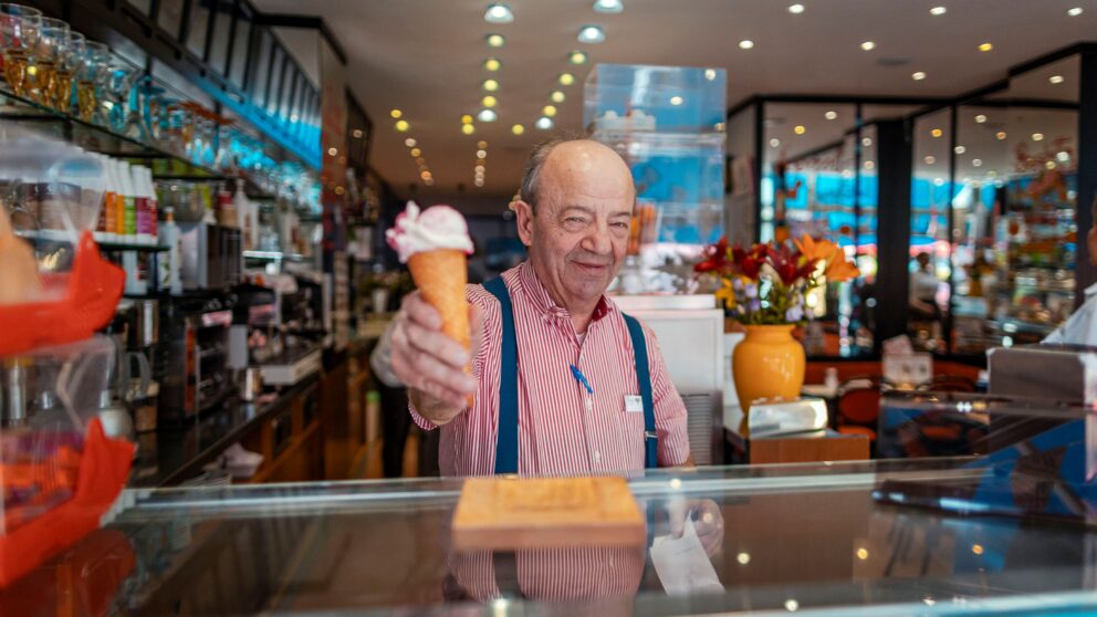 Roberto, Inhaber des Eiscafés Stefan da Roberto am Worringer Platz, ist hinter der Eisverkaufstheke und gibt ein Eis heraus.